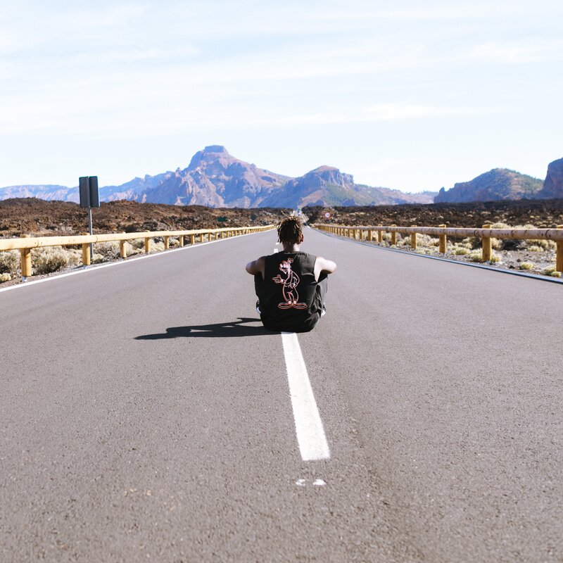 man sitting in the middle of an empty desert road